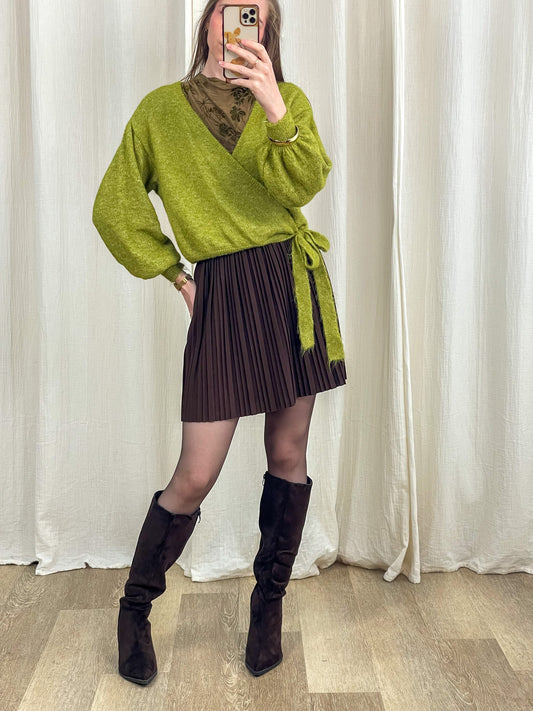 Jupe courte plissée marron taille haute femme portée avec pull cache-cœur vert et bottes hautes