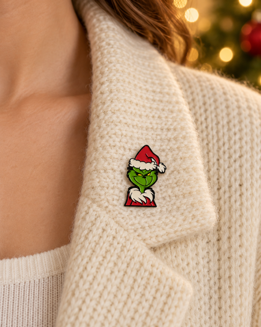 Pin's Grinch Noël vert et rouge avec bonnet Père Noël porté sur pull beige tricoté accessoire festif humoristique
