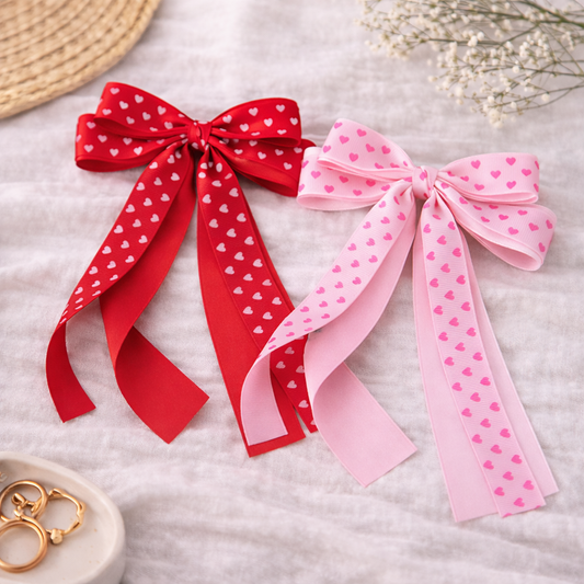 Deux barrettes nœud en ruban à motifs cœurs, posées sur un fond lifestyle doux et lumineux, accessoires cheveux romantiques