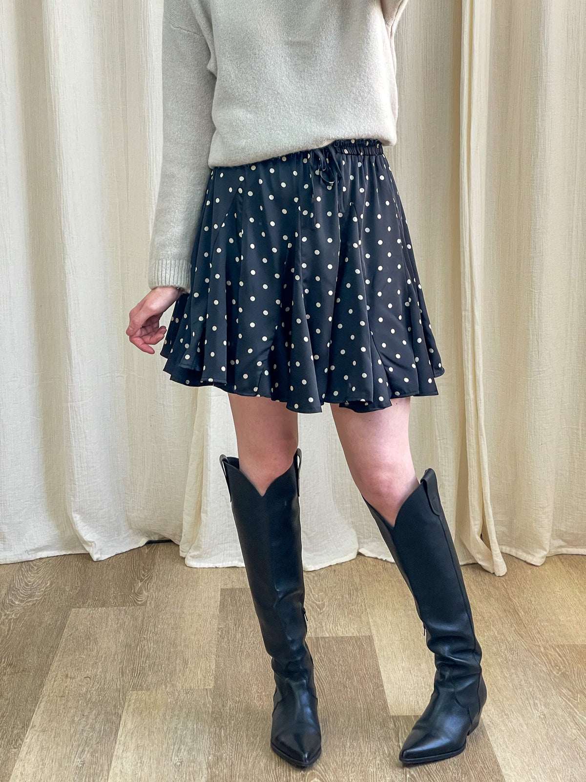Jupe patineuse noire à pois blancs taille élastique femme style rétro chic portée avec pull beige et bottes western