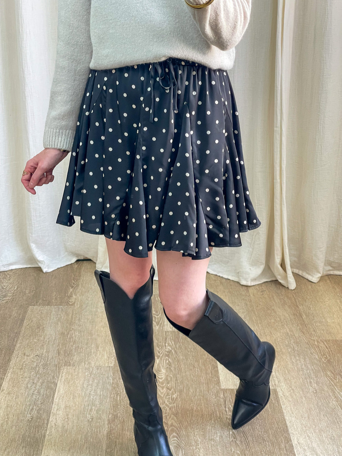 Jupe patineuse noire à pois blancs taille élastique femme associée à pull beige et bottes western noires