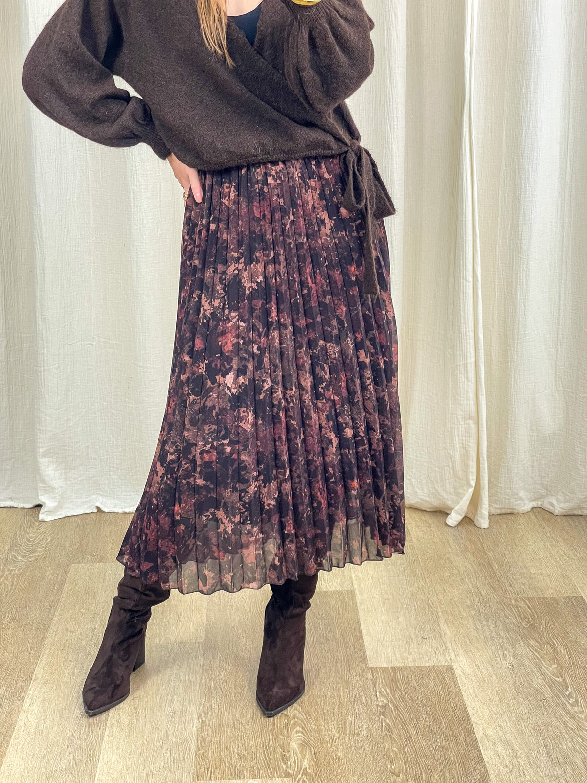 Jupe midi plissée imprimé floral bordeaux et noir femme avec pull cache-cœur marron et bottes hautes