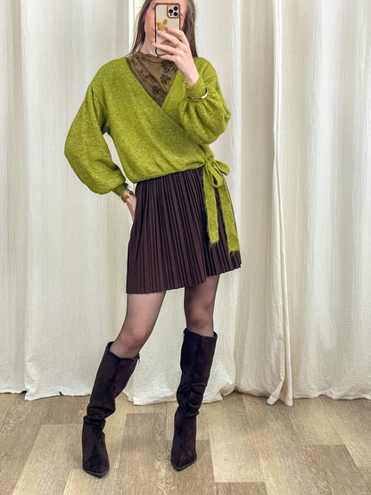 Jupe courte plissée marron taille haute femme portée avec pull cache-cœur vert et bottes hautes