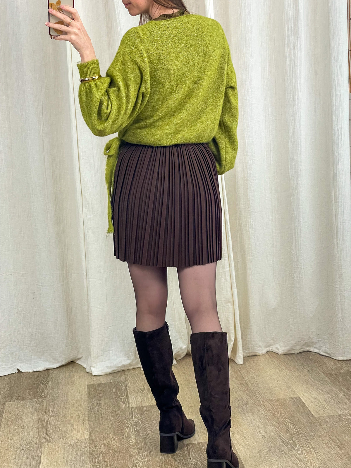 Jupe courte plissée marron taille haute élastique femme portée avec pull vert et bottes hautes noires