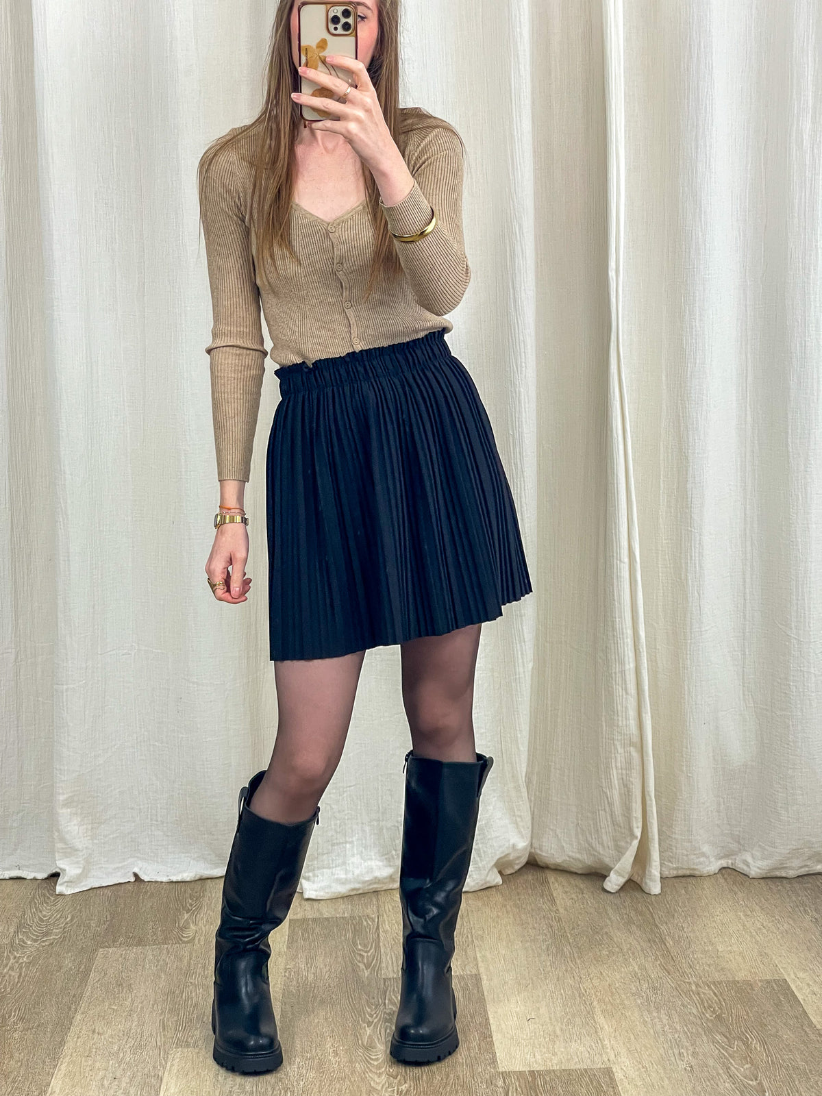 Jupe courte plissée noire taille haute élastique portée avec cardigan beige et bottes cavalières femme