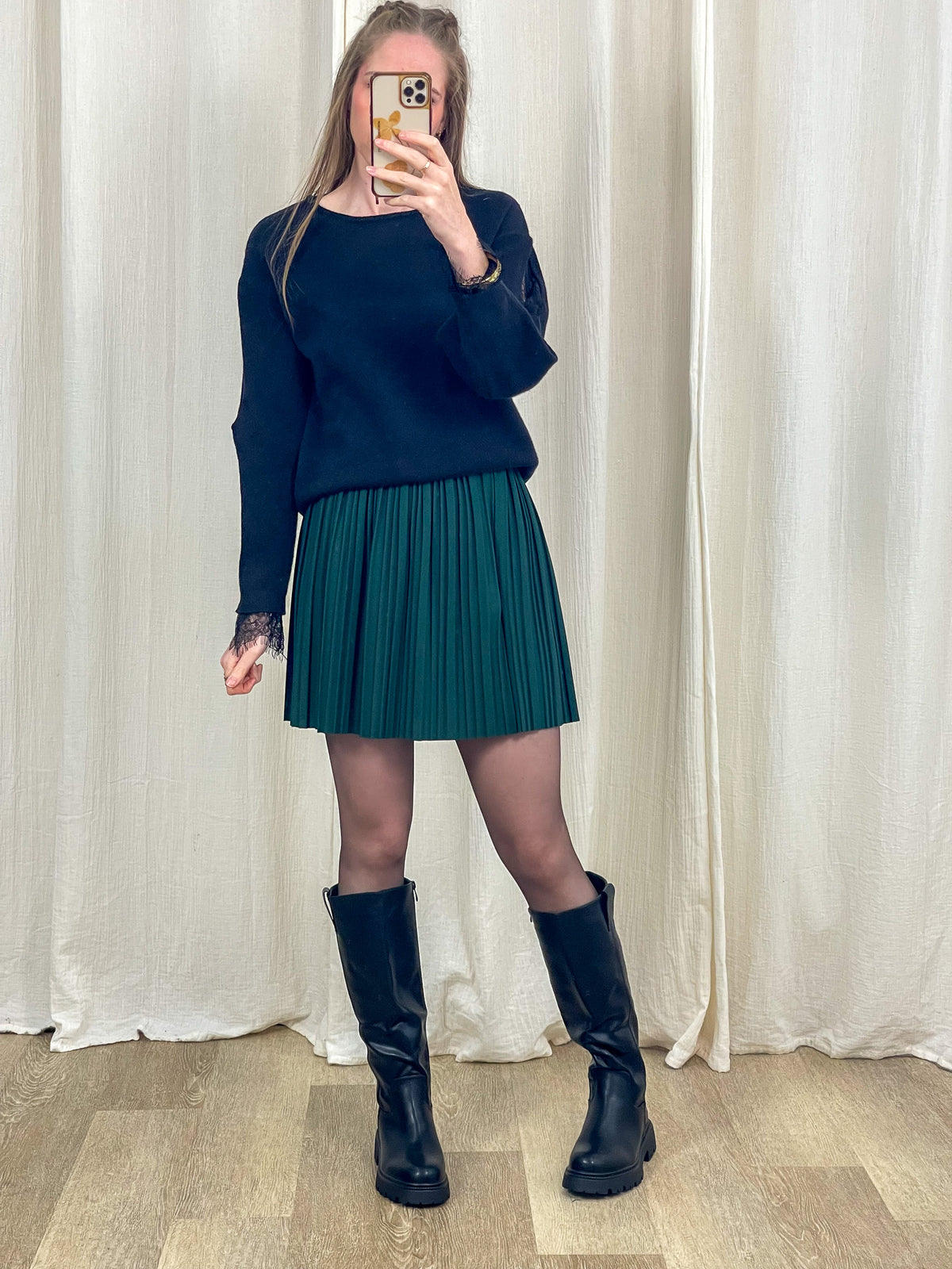 Jupe courte plissée vert sapin taille haute élastique portée avec pull noir et bottes femme
