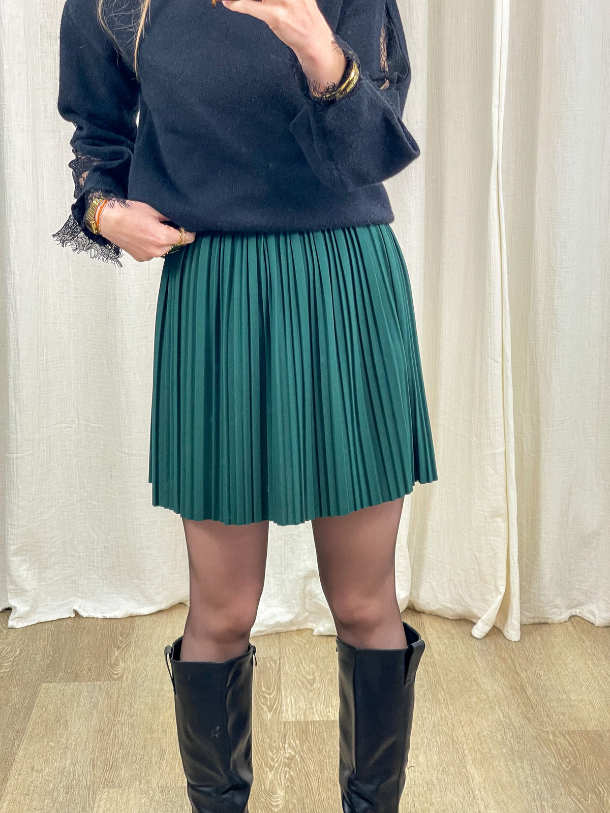 Jupe courte plissée verte taille haute élastique portée avec pull noir et bottes femme hiver