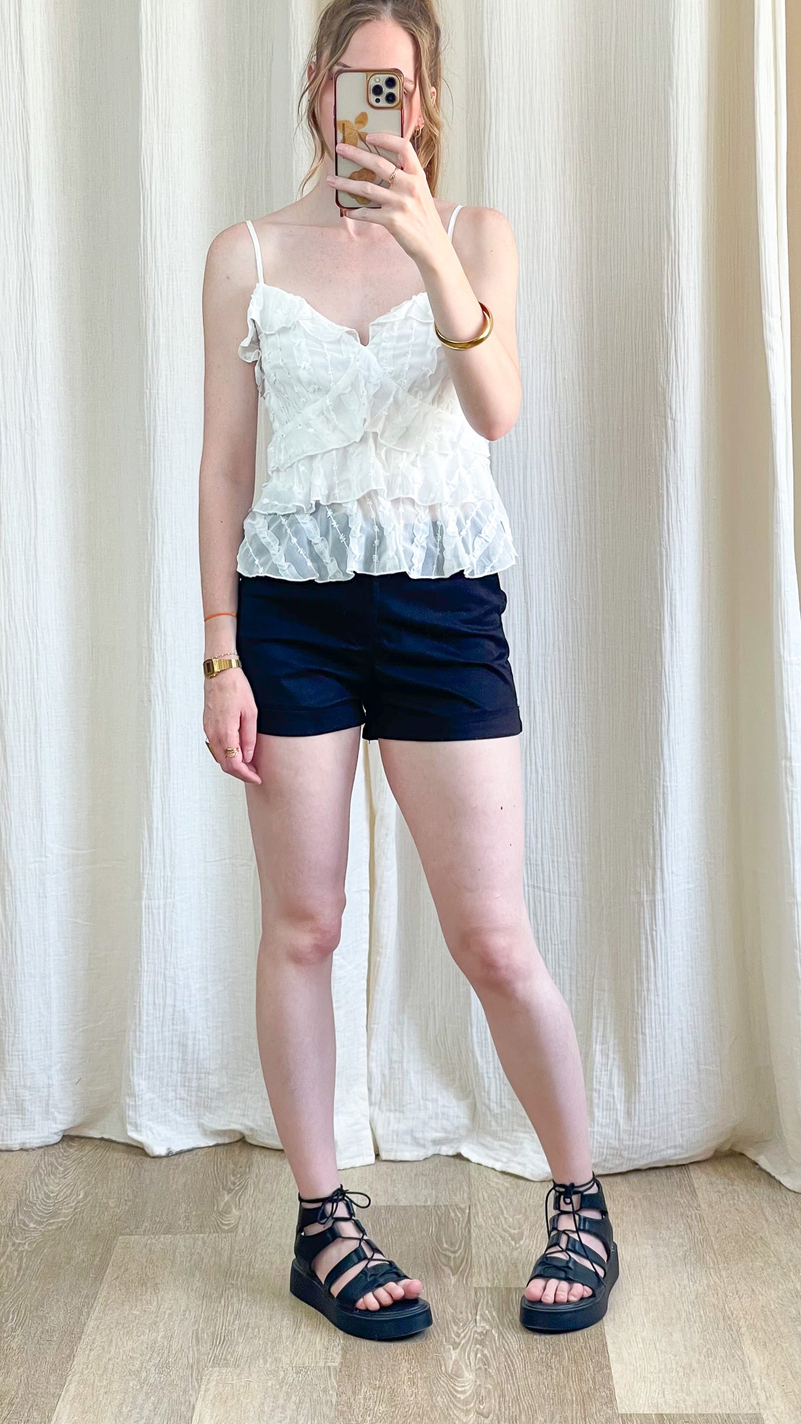 Top blanc à volants et bretelles fines style romantique femme, associé à un short bleu marine et sandales noires