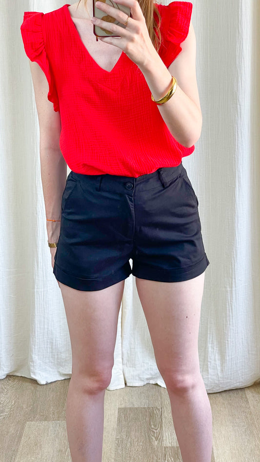 Short noir taille haute femme coupe ajustée avec revers, porté avec top rouge à volants, look casual chic été