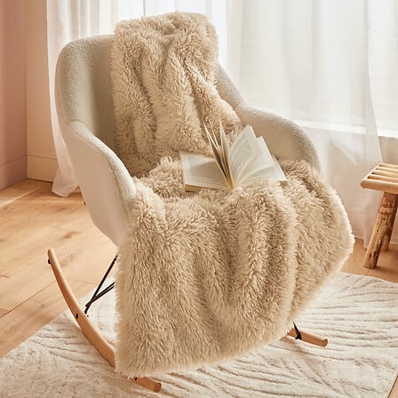 Plaid beige fausse fourrure douce Duvia 120x150cm posé sur fauteuil, couverture cocooning décoration intérieure