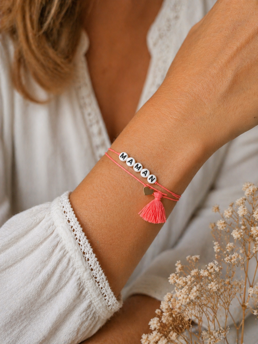 Bracelet affectif Maman porté au poignet — cordon corail, perles lettres blanches et pompon corail avec breloque cœur doré