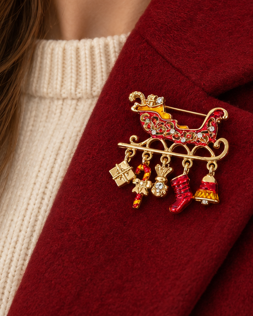 Broche traineau de Noël dorée et rouge avec breloques cadeau, chaussette et cloche sur manteau bordeaux femme