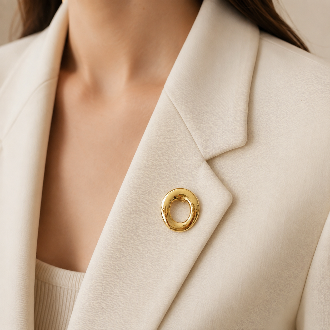 Broche cercle doré effet miroir portée sur blazer écru femme, bijou minimaliste tendance accessoire mode élégant