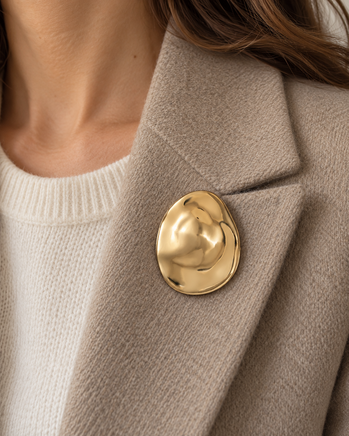 Broche ovale dorée effet froissé organique portée sur blazer beige, accessoire bijou fantaisie femme tendance