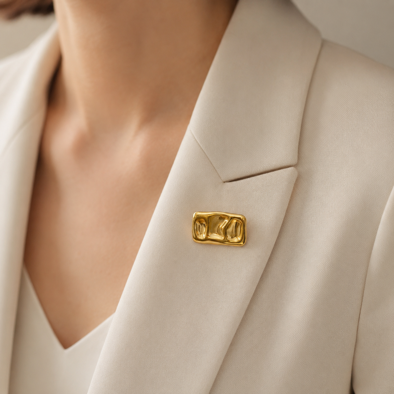 Broche dorée rectangulaire relief organique sculptural portée sur blazer crème femme accessoire tendance