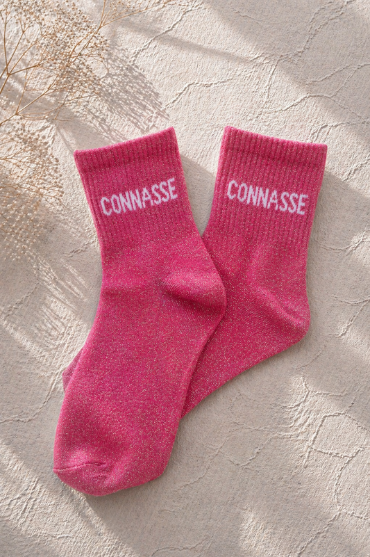 Chaussettes pailletées rose avec inscription CONNASSE brodée en blanc sur fond clair texturé