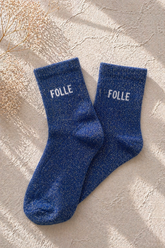 Chaussettes pailletées bleu avec inscription FOLLE brodée en blanc sur fond clair texturé