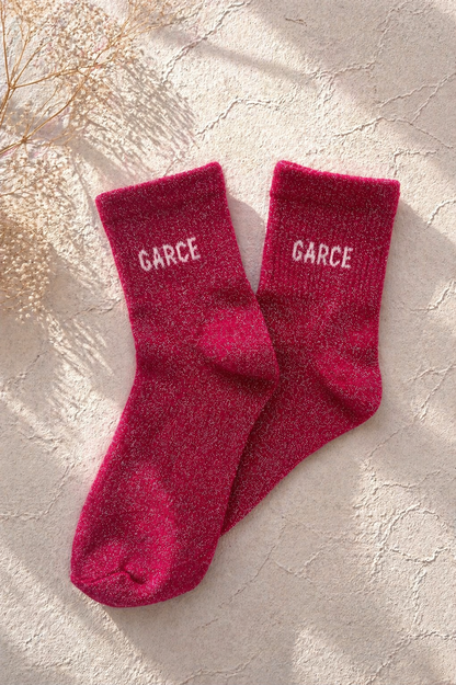 Chaussettes pailletées rose fuchsia avec inscription GARCE brodée en blanc sur fond clair texturé