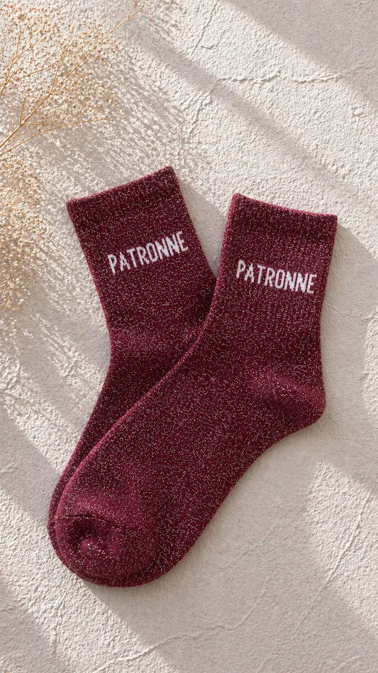 Chaussettes pailletées bordeaux avec inscription PATRONNE brodée en blanc sur fond clair texturé