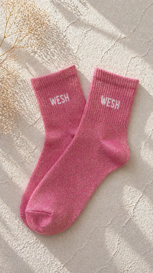 Chaussettes pailletées rose avec inscription WESH brodée en blanc sur fond clair texturé
