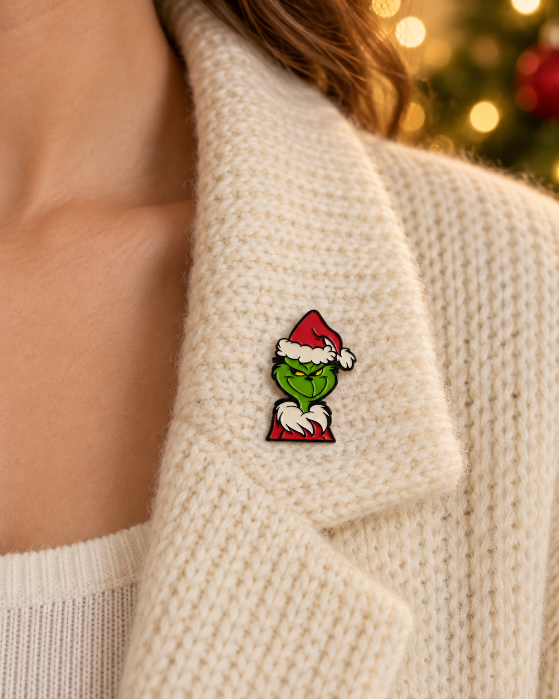 Pin's Grinch Noël vert et rouge avec bonnet Père Noël porté sur pull beige tricoté accessoire festif humoristique
